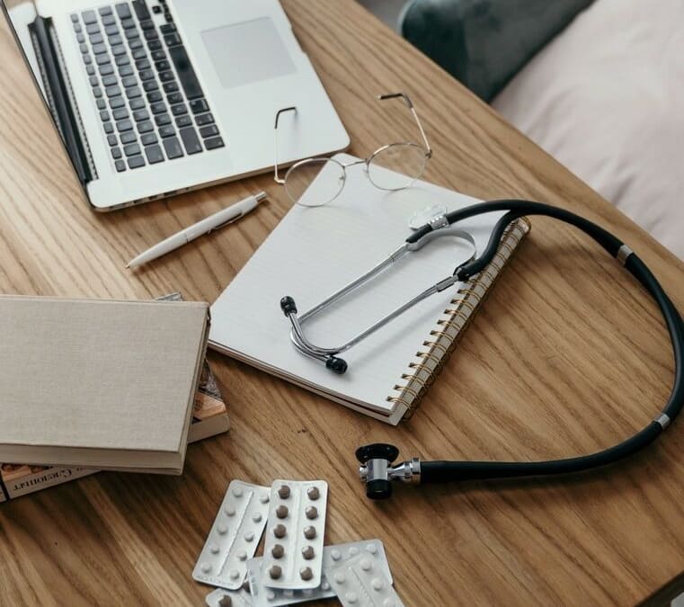 desk of a naturopathic doctor with a laptop, glasses, medicines and stethoscope on it